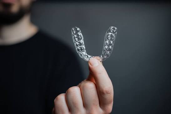 A man holding a single clear aligner between finger and thumb.