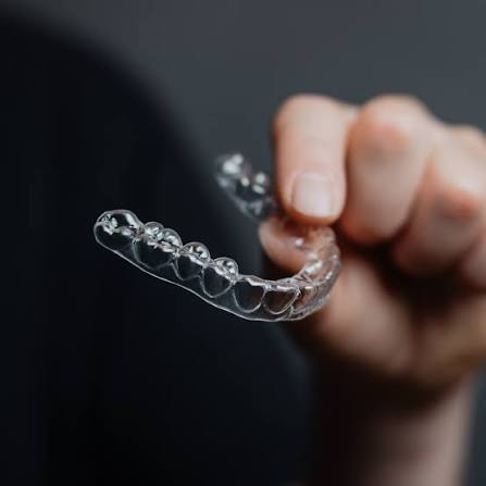 A hand holding a single clear aligner against a dark background.